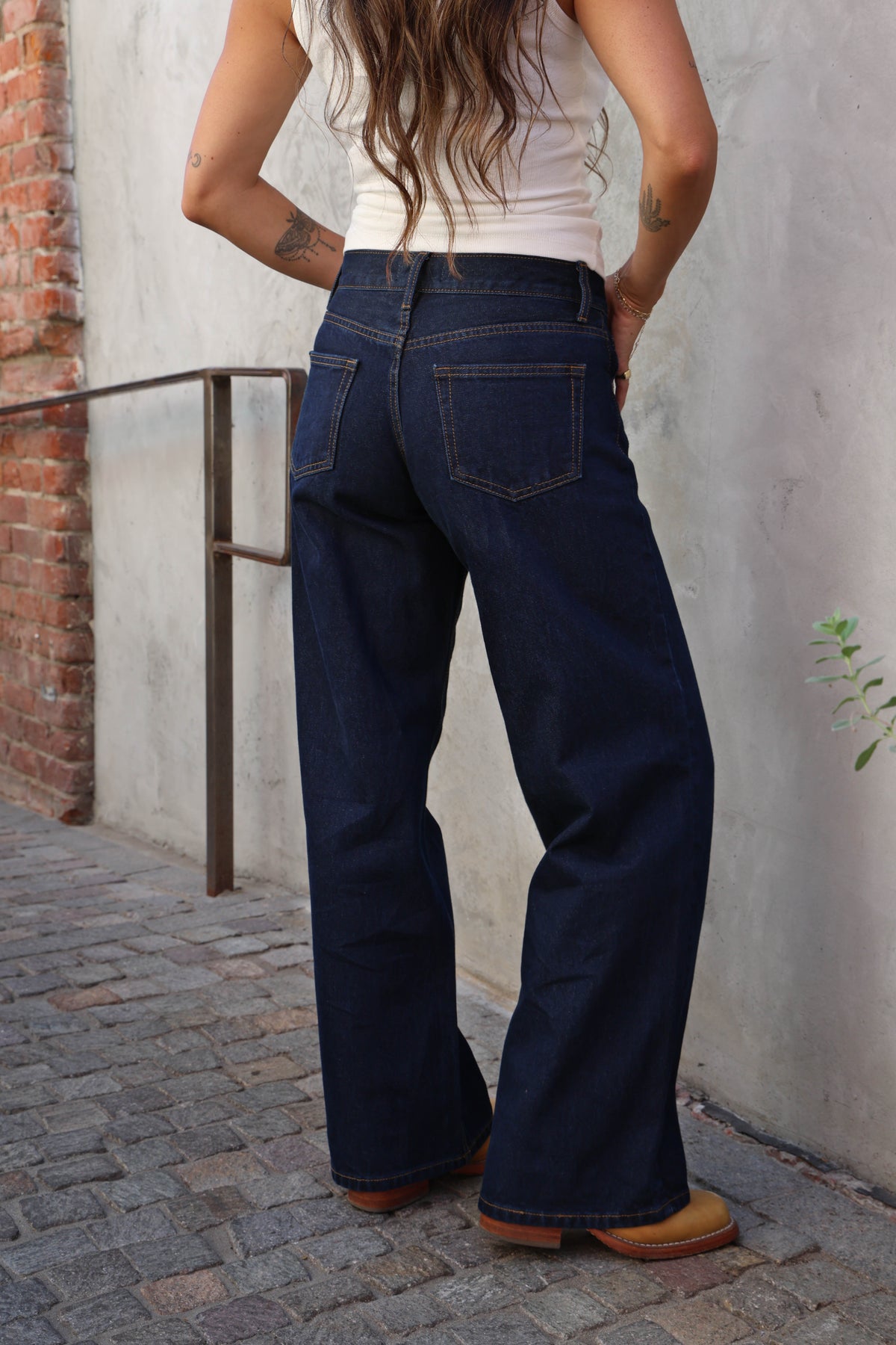 Woman wearing jeans and a white tank against a grey background.