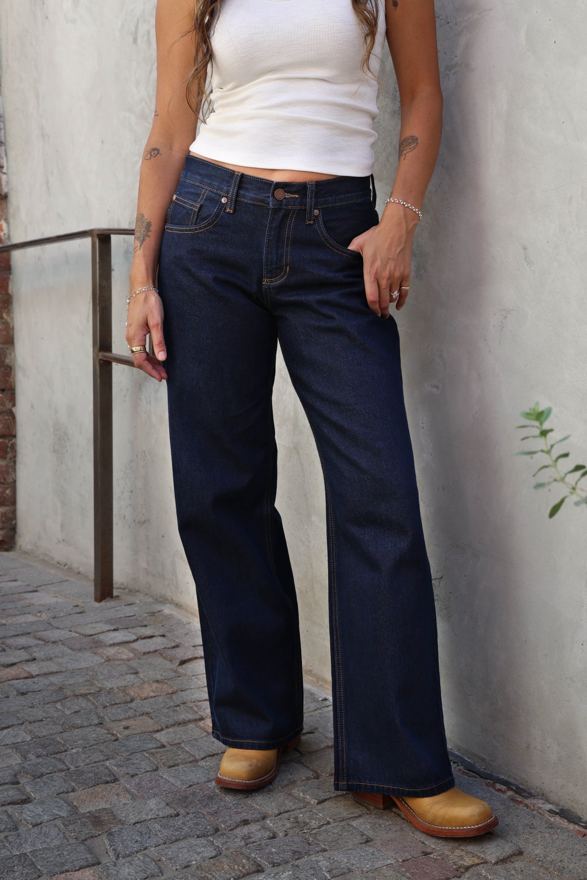 Woman wearing jeans and a white tank against a grey background.