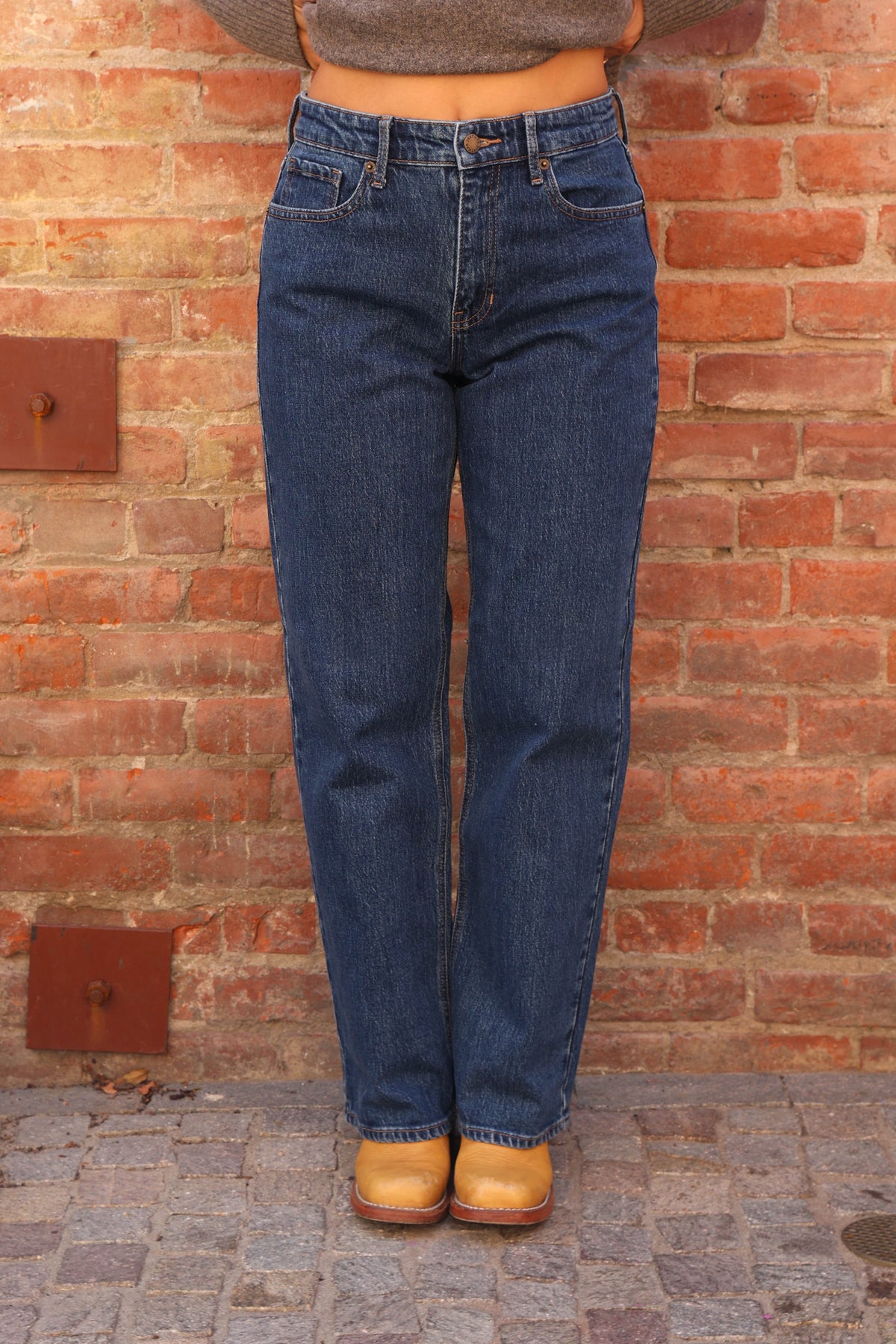 Woman wearing jeans and boots against a brick wall.