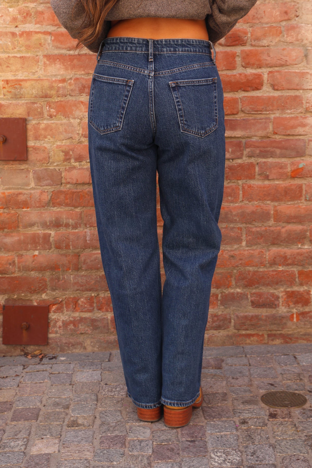 Woman wearing jeans and boots against a brick wall.