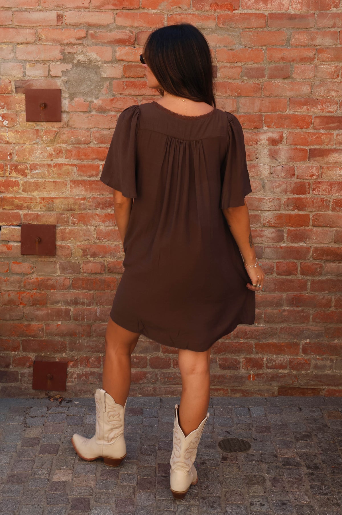 Woman wearing a brown dress against a brick wall.