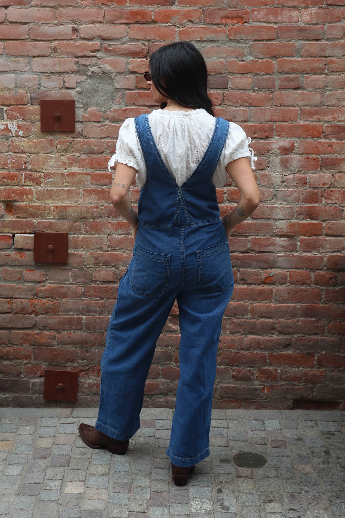 Woman wearing a pair of overalls with a white blouse against a brick wall