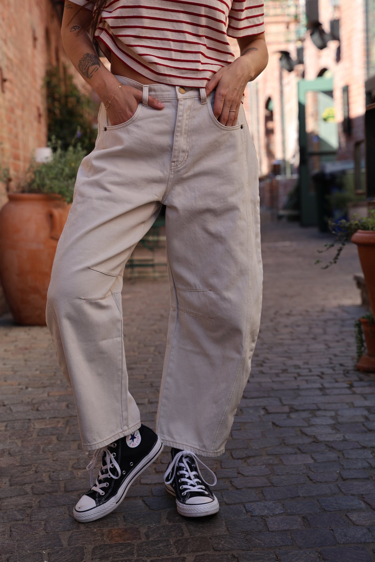 Person wearing light-colored pants and black sneakers standing on a stone pavement.
