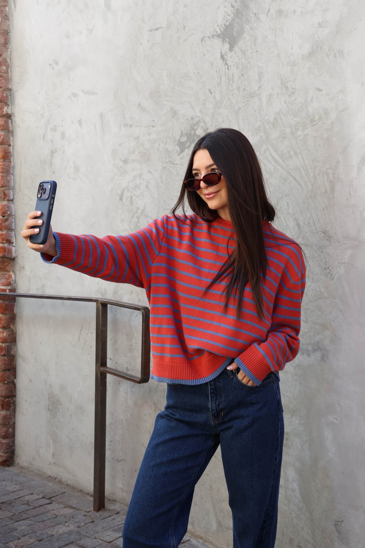 Woman wearing a striped sweater with jeans standing against a plain wall.
