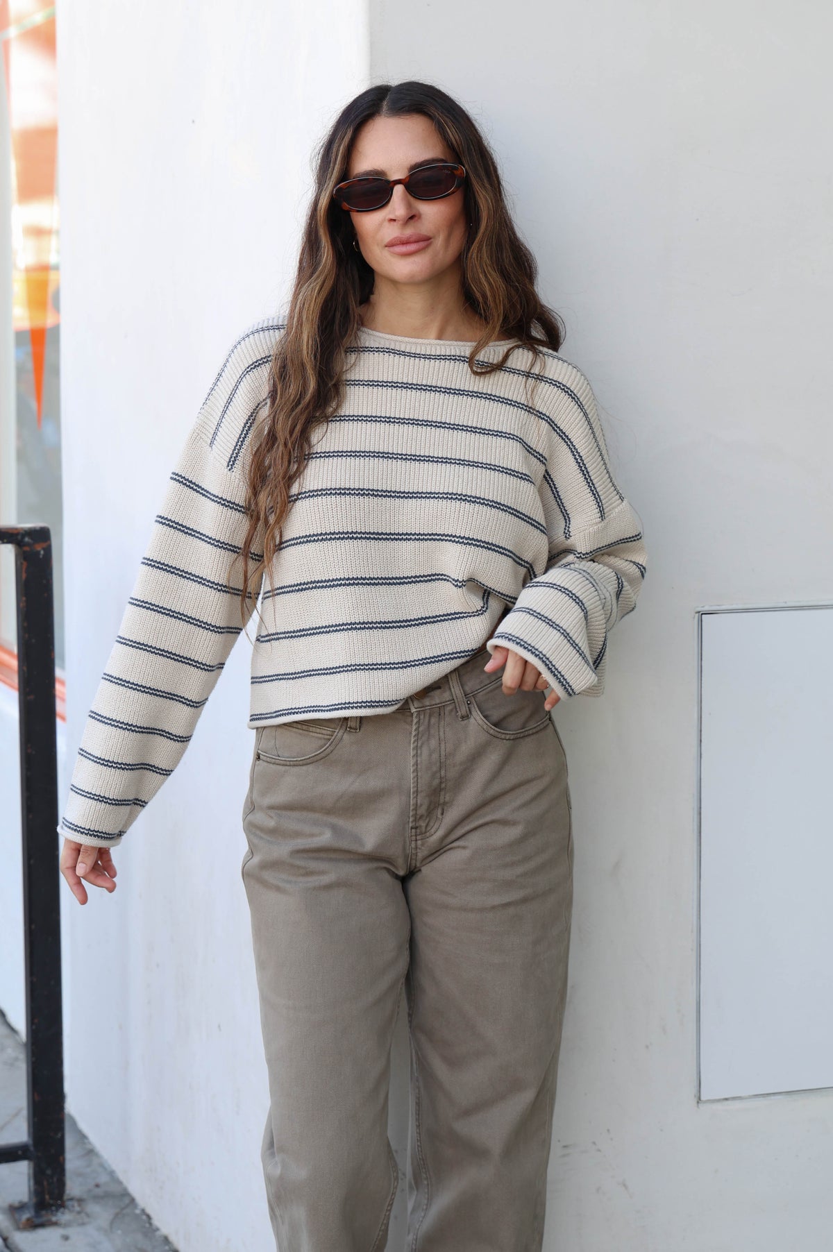 Woman wearing a striped sweater, olive pants and sunglasses.