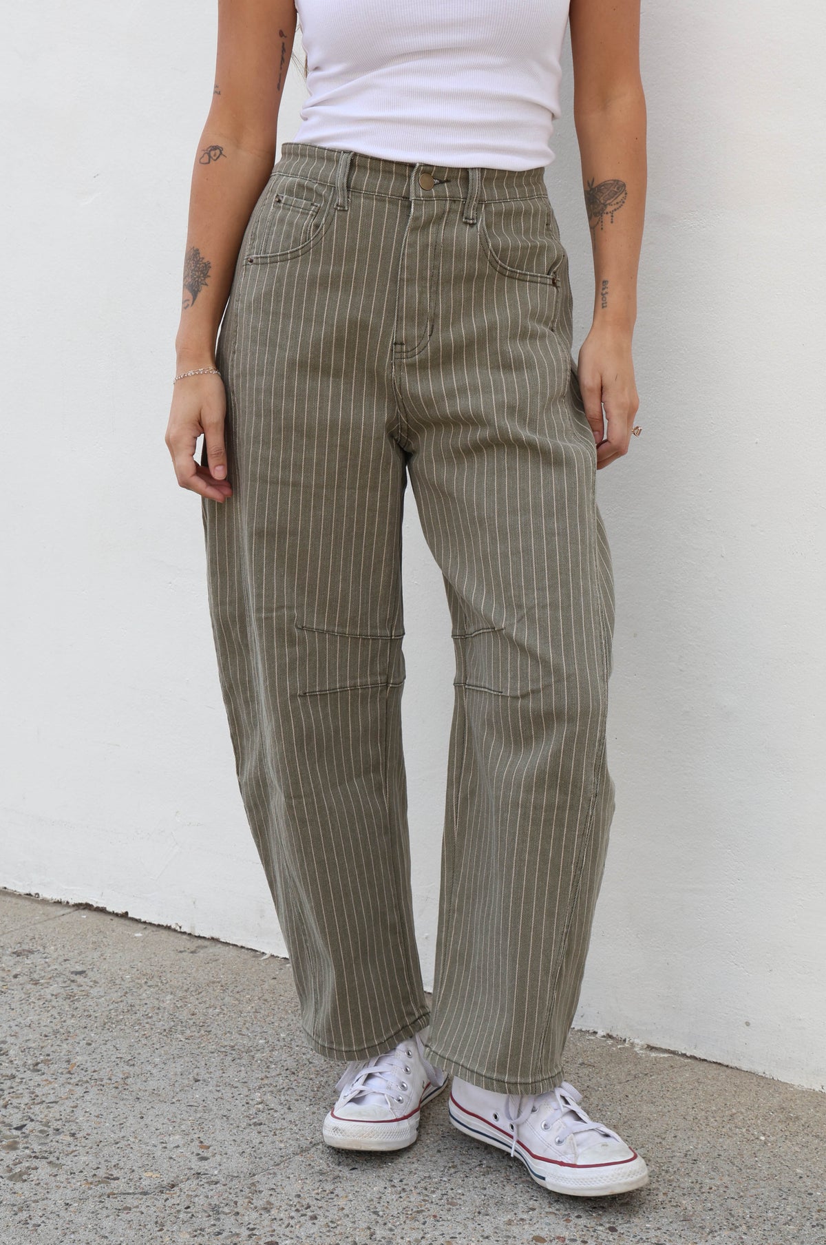 Woman wearing striped olive pants against a plain wall.