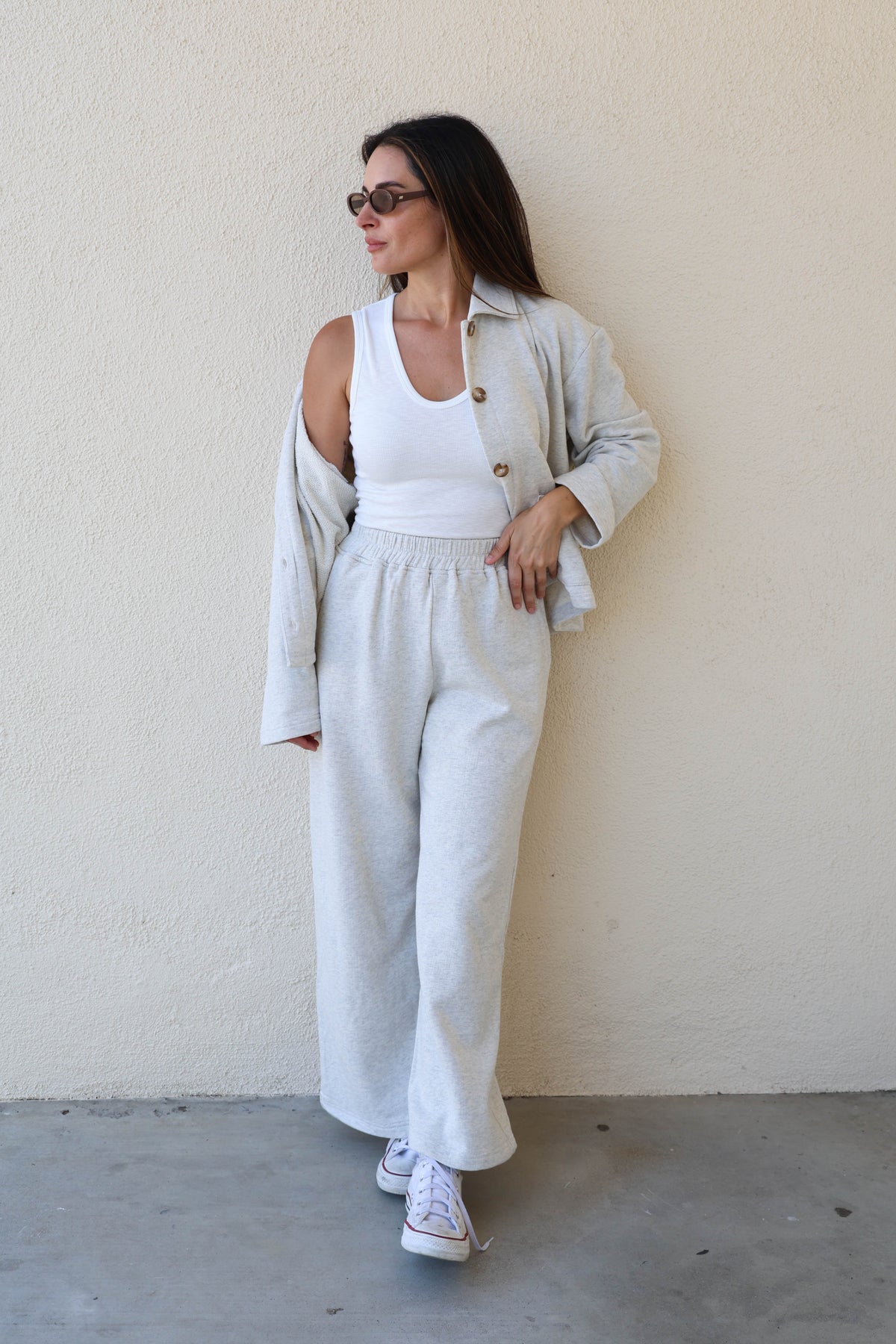 Woman wearing a grey sweat jacket against a plain wall.