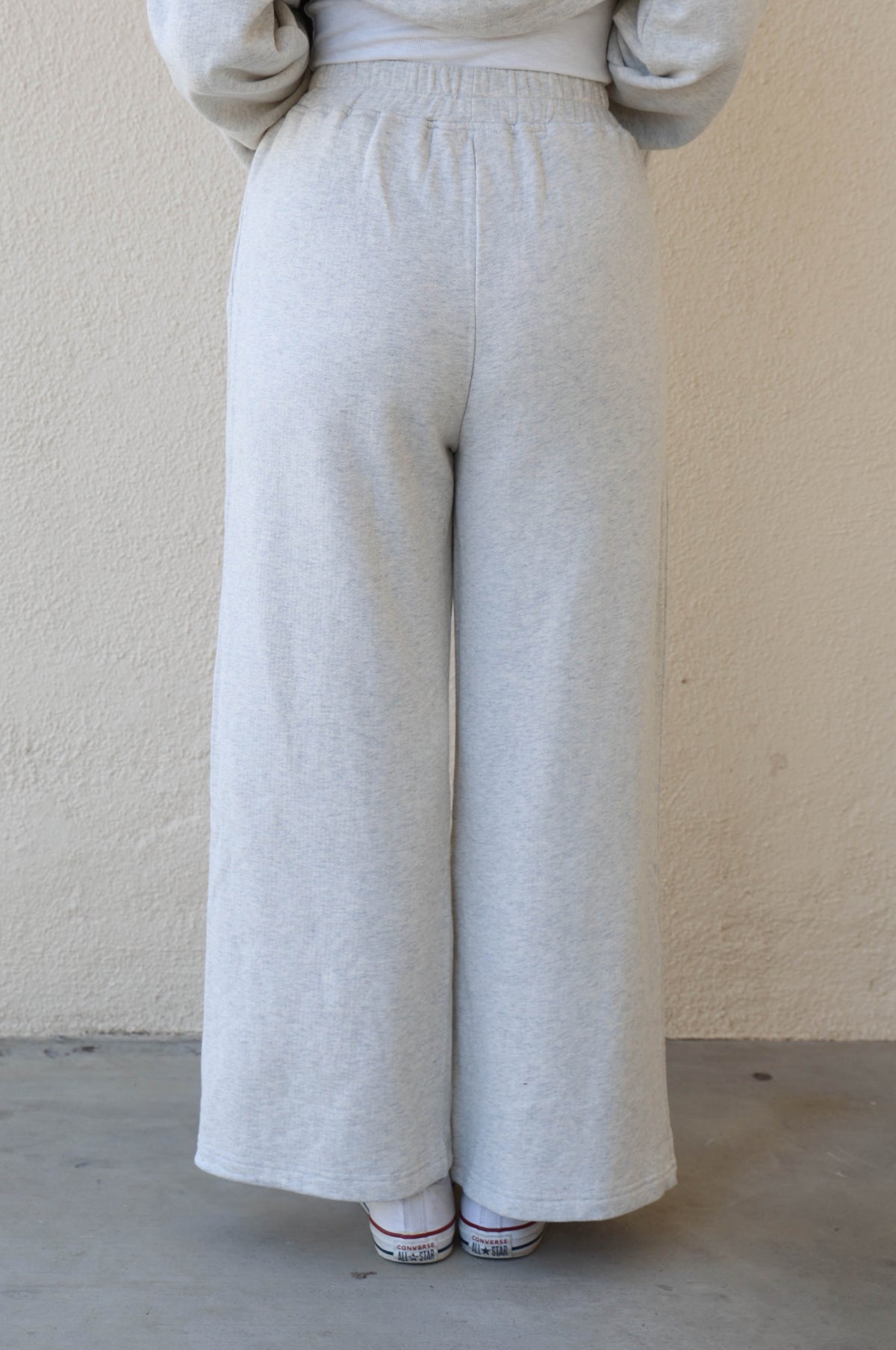 Woman wearing grey sweatpants against a plain wall.