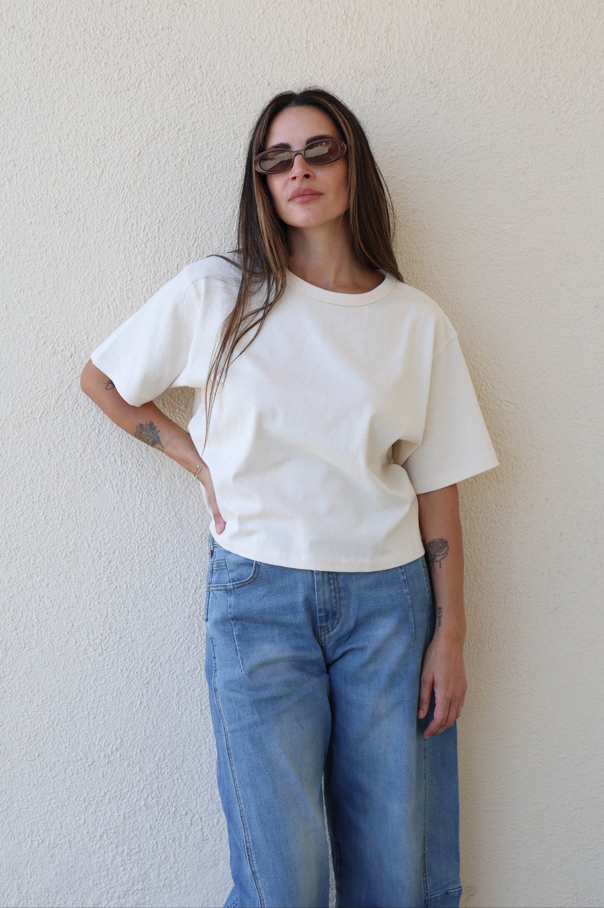 Woman wearing a plain tee and jeans against a plain wall.