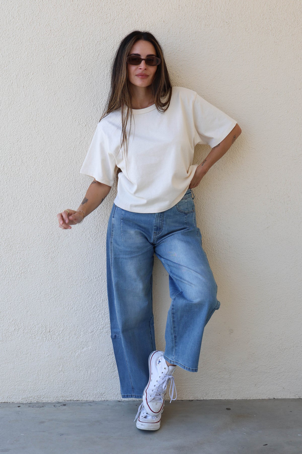 Woman modeling a pair of barrel jeans against a plain background.