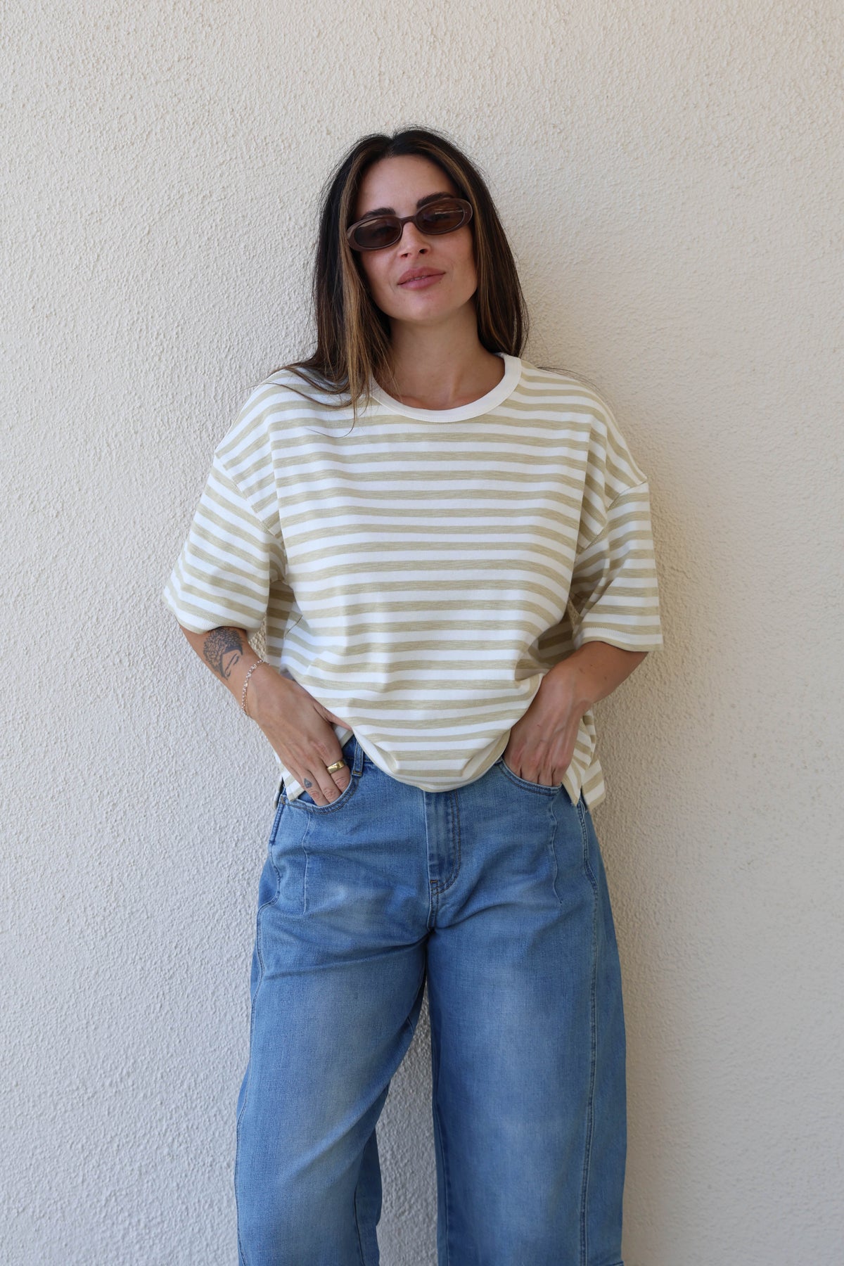 Woman wearing a striped tee with jeans against a plain wall.