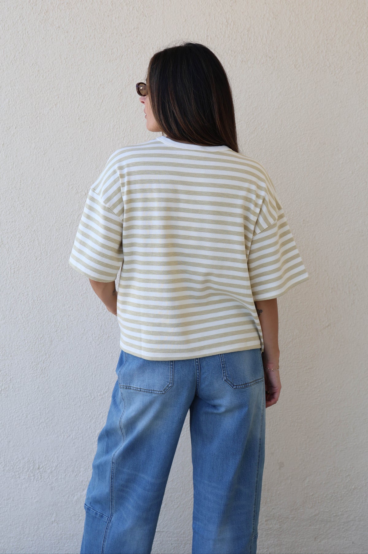 Woman wearing a striped tee with jeans against a plain wall.