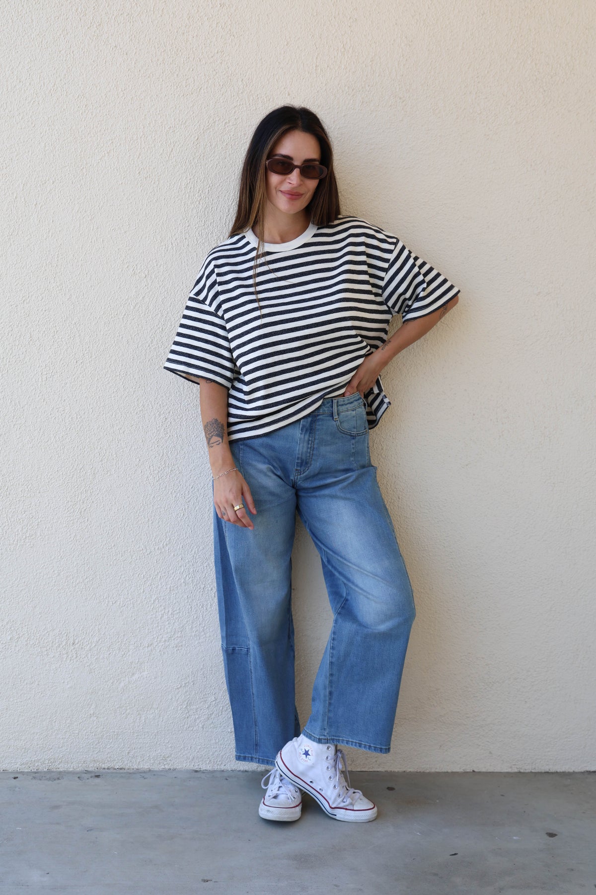 Woman wearing a striped tee and jeans against a plain wall.
