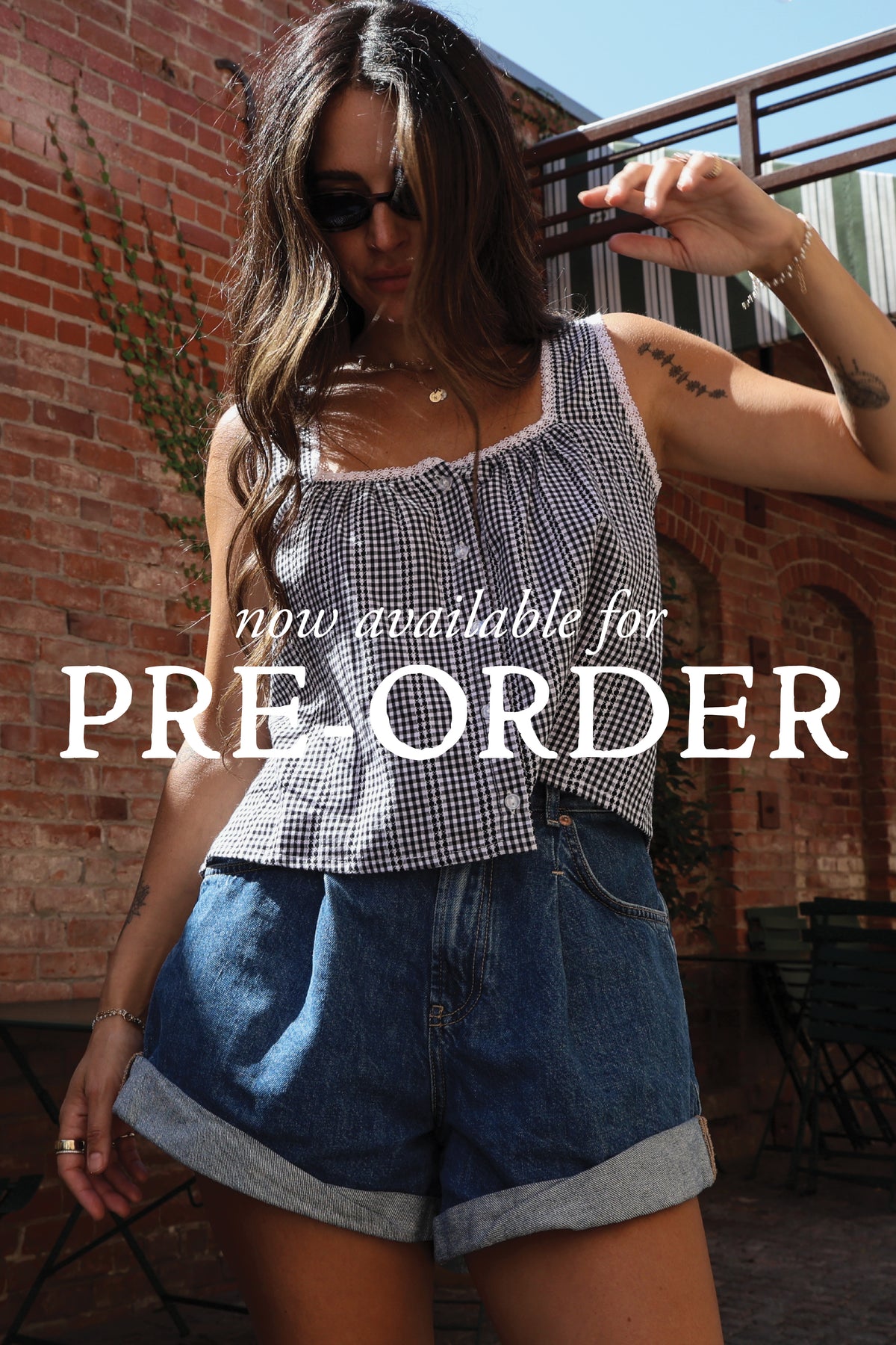 "Now available for Pre-Order" text across the image. Woman wearing a gingham top and shorts standing against a brick wall.