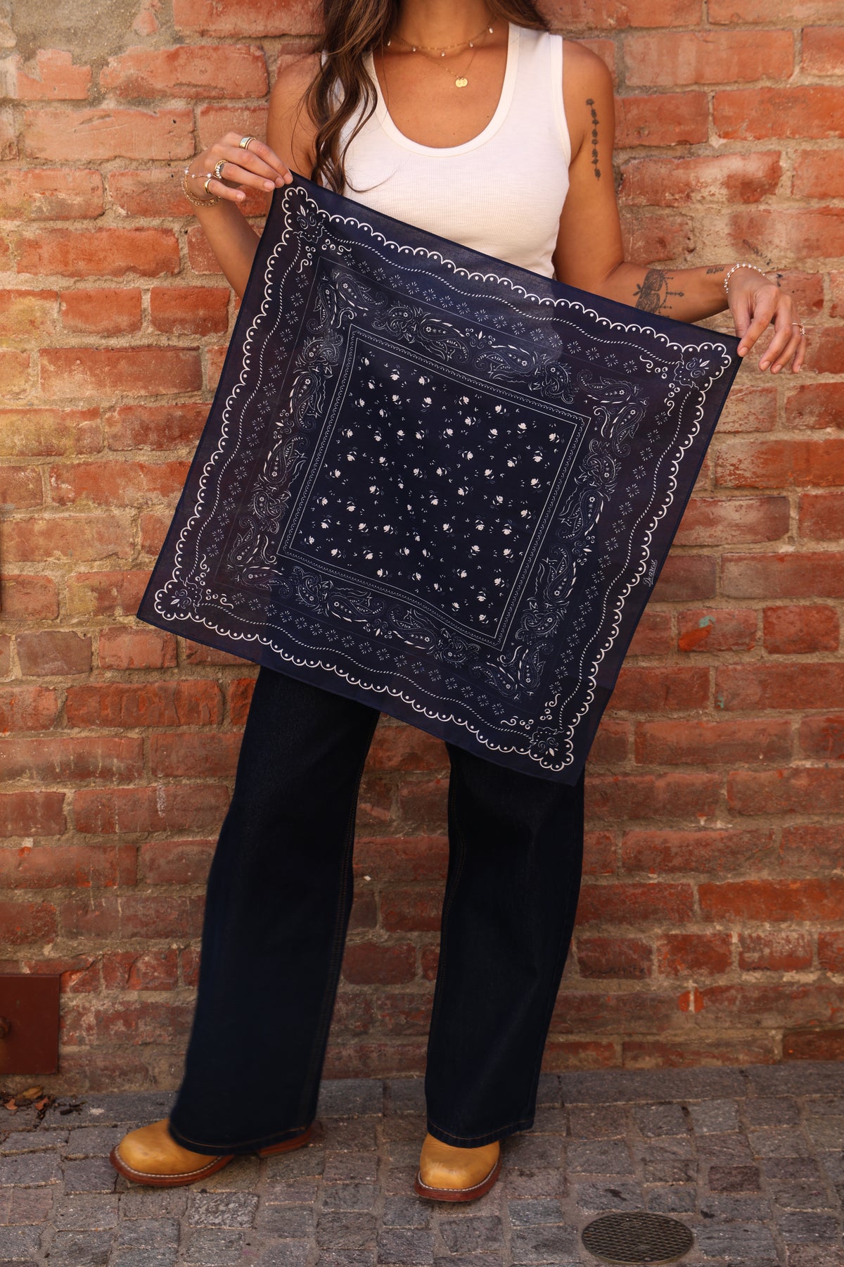 Woman standing holding a bandana against a brick wall.