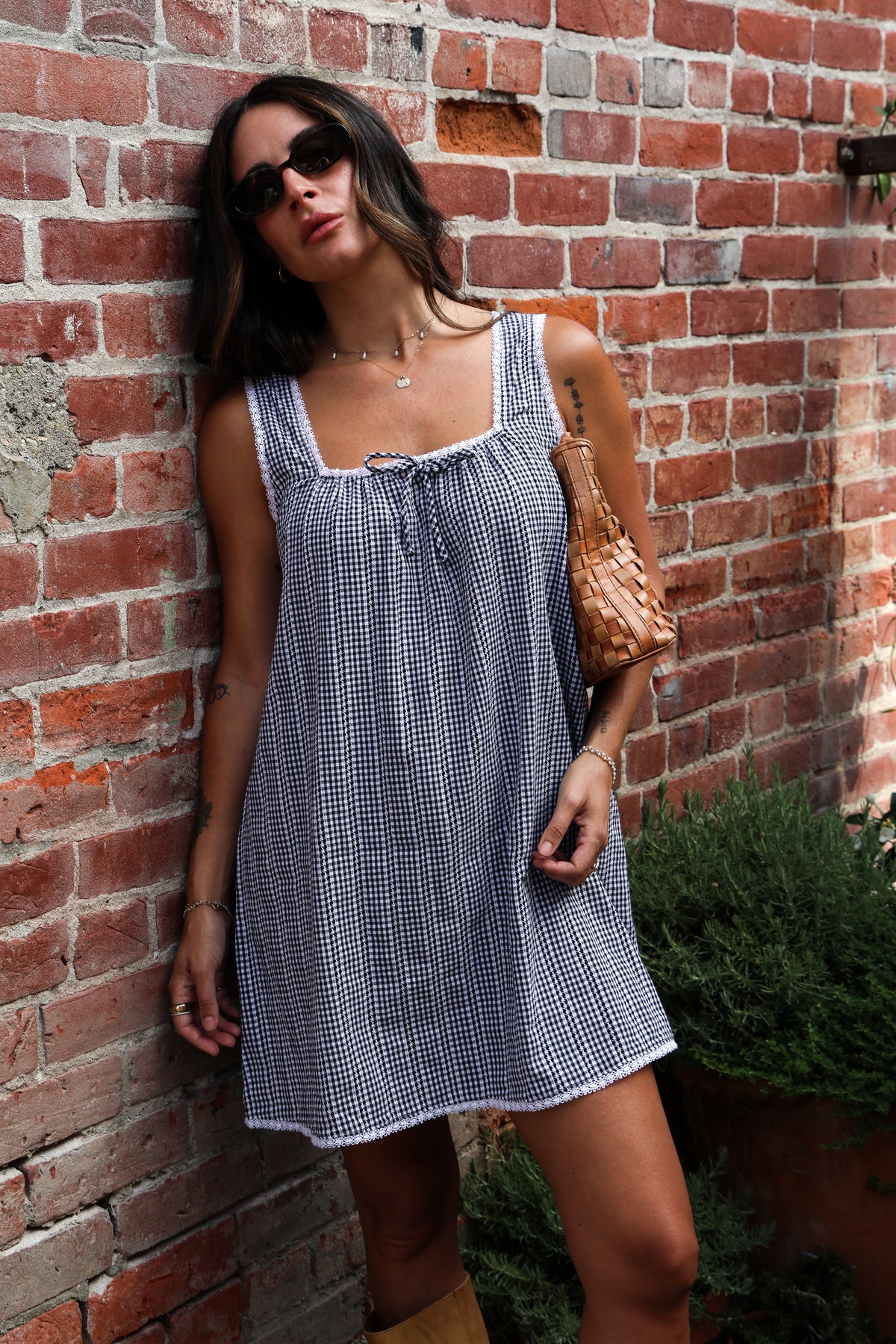 Woman wearing a gingham dress standing against a brick wall.