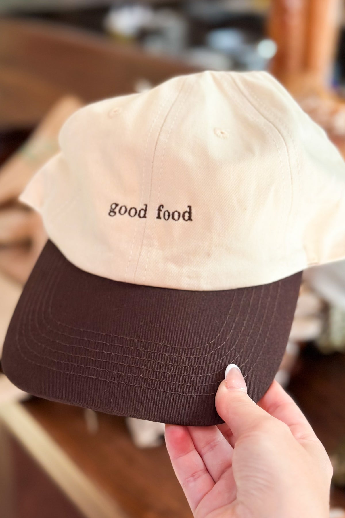 Cap with 'good food' text held by a hand in an indoor setting