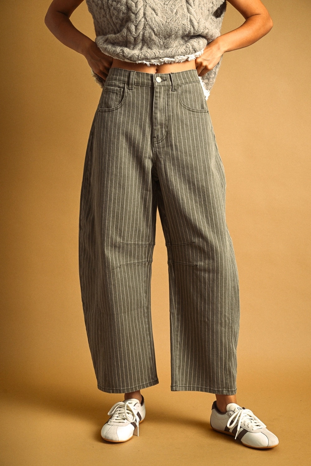 Woman wearing olive barrel jeans against a plain background.