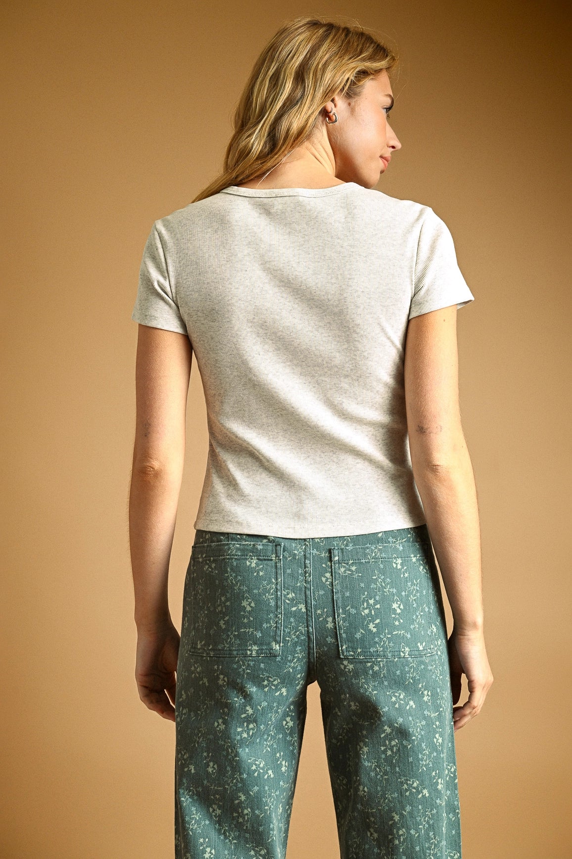 Woman wearing a white t-shirt and teal patterned pants on a beige background