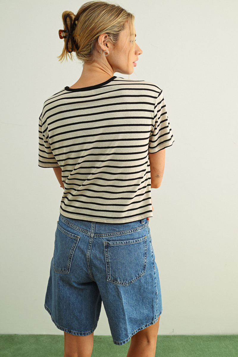 Person wearing a striped shirt and denim shorts against a plain background