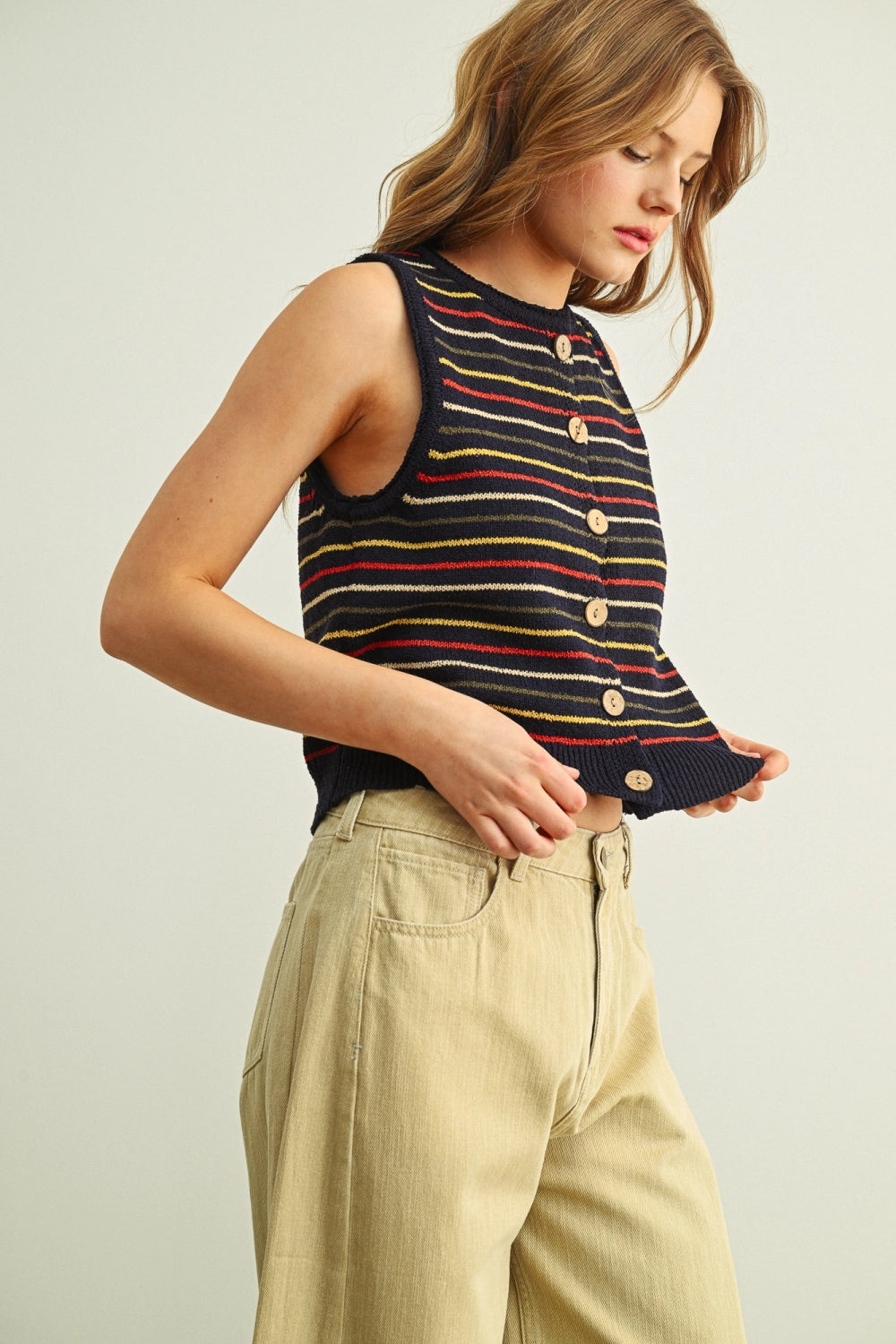 Woman wearing a striped sleeveless top and beige pants on a plain background