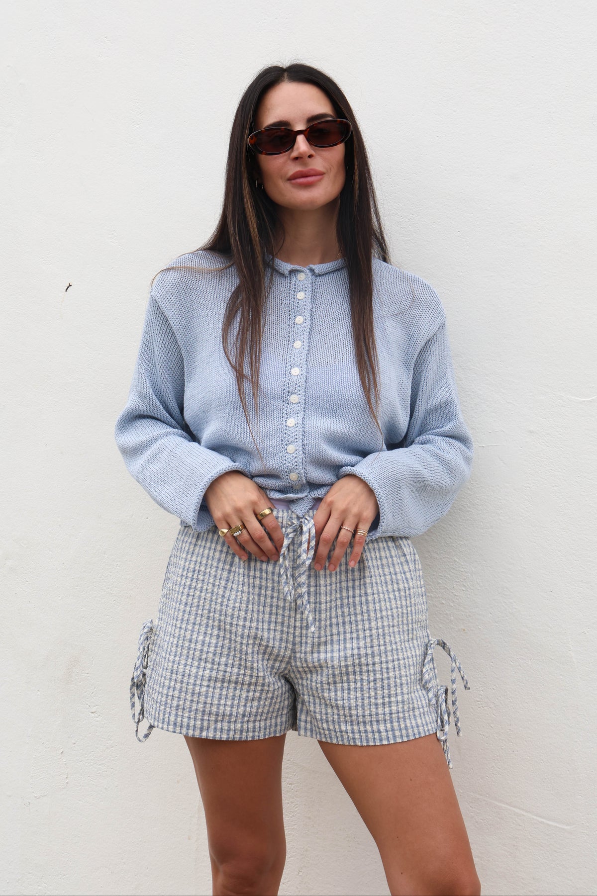 Woman wearing a light blue shirt and checkered shorts against a white background