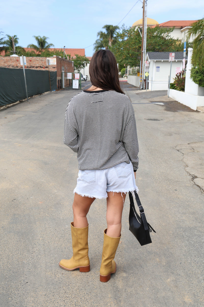 A woman wearing a black and white striped long-sleeve t-shirt and light wash denim shorts, standing on an outdoor street.