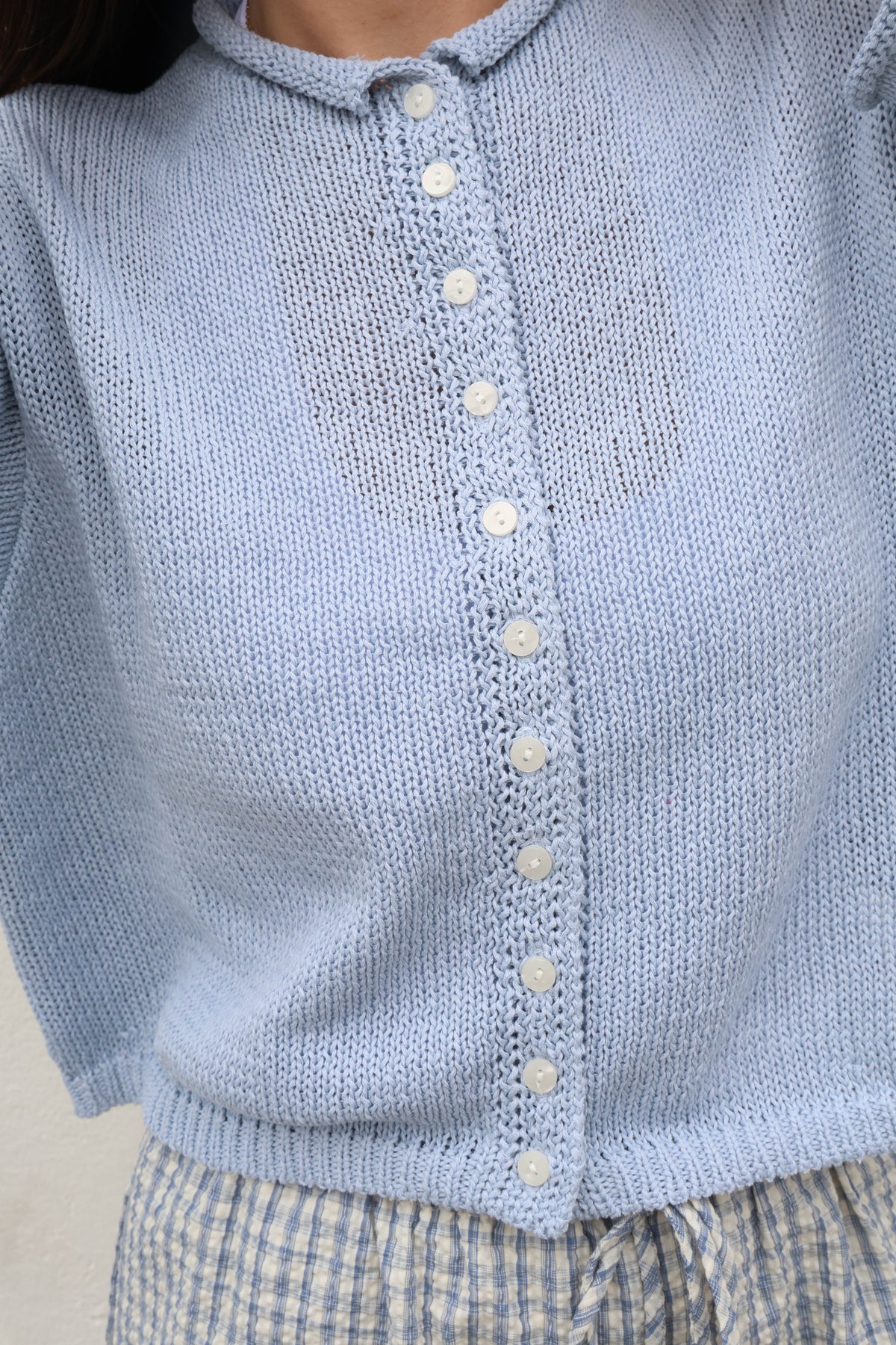 Light blue knitted cardigan with button details on a neutral background