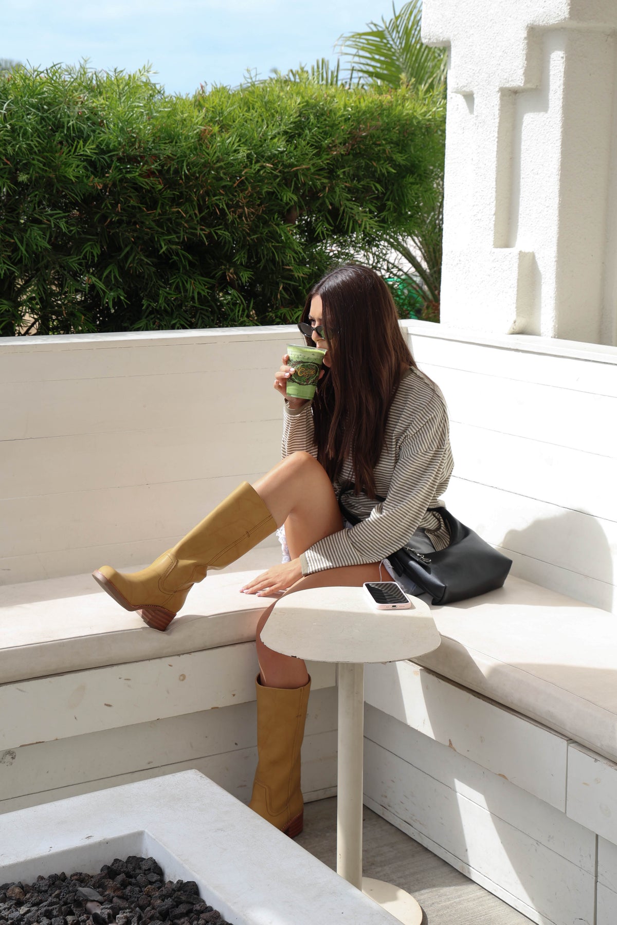 Woman wearing a striped long sleeve shirt with jean shorts and boots sitting down at a cafe.