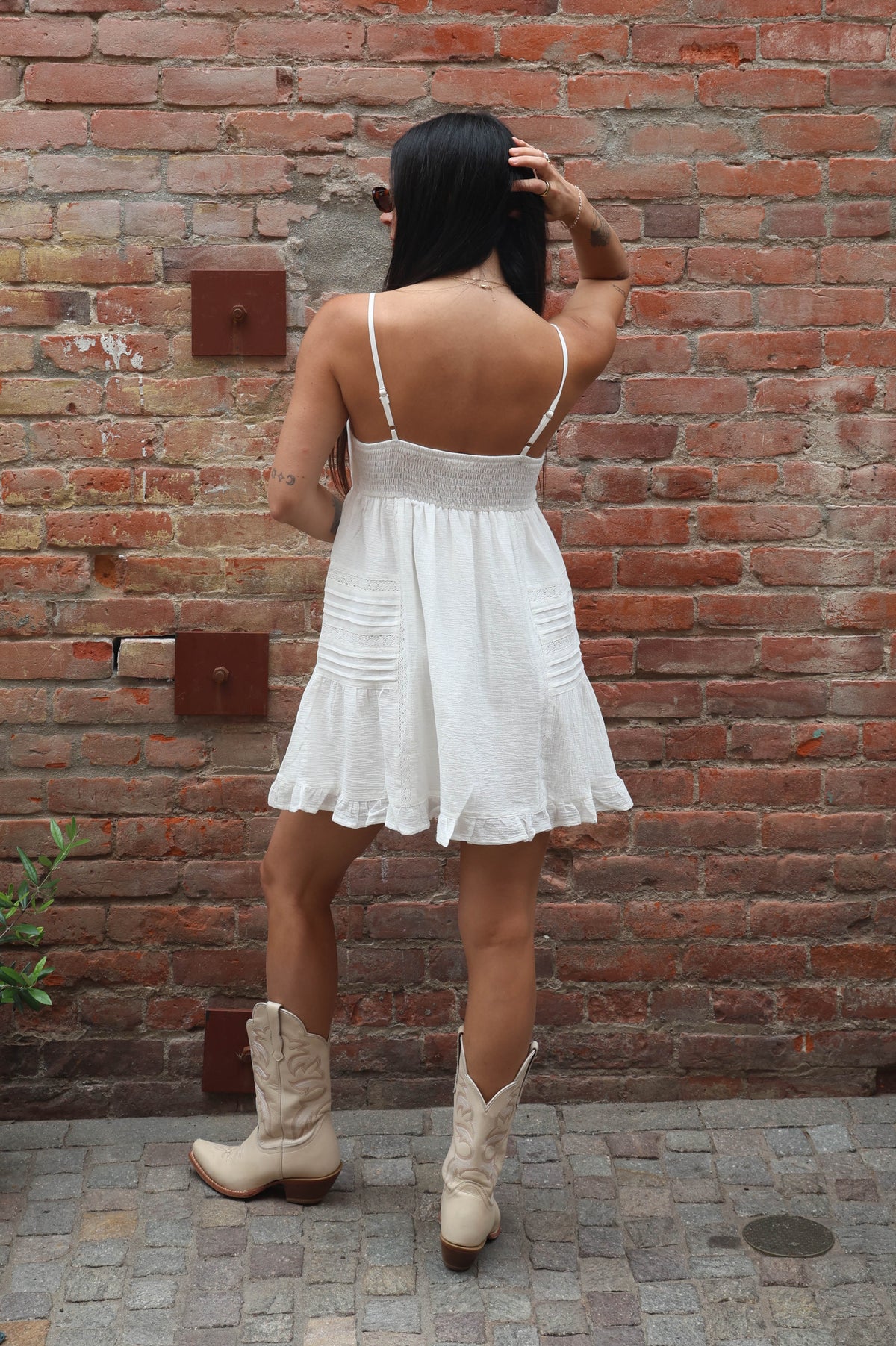 Person wearing a white dress and beige cowboy boots against a brick wall.