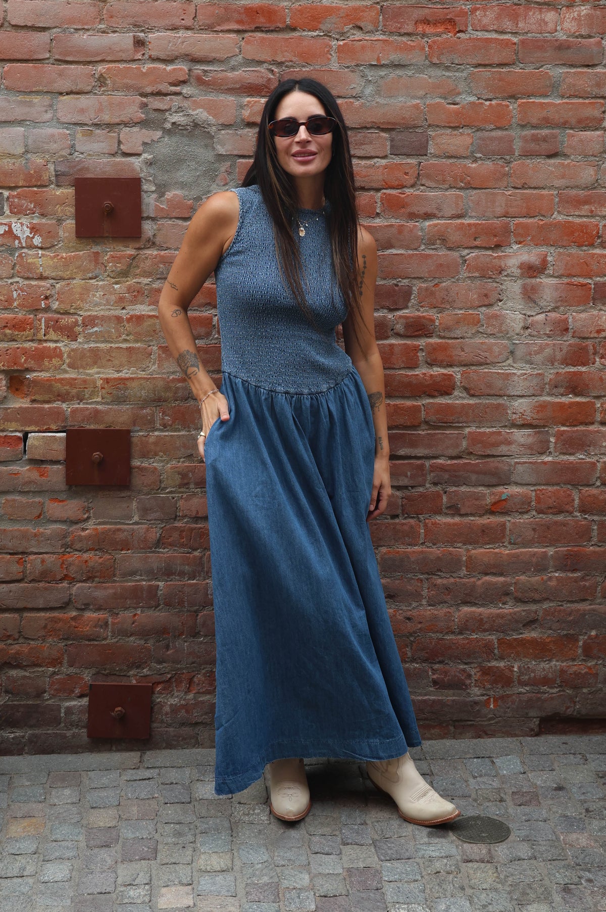 Woman in a blue dress standing against a brick wall.