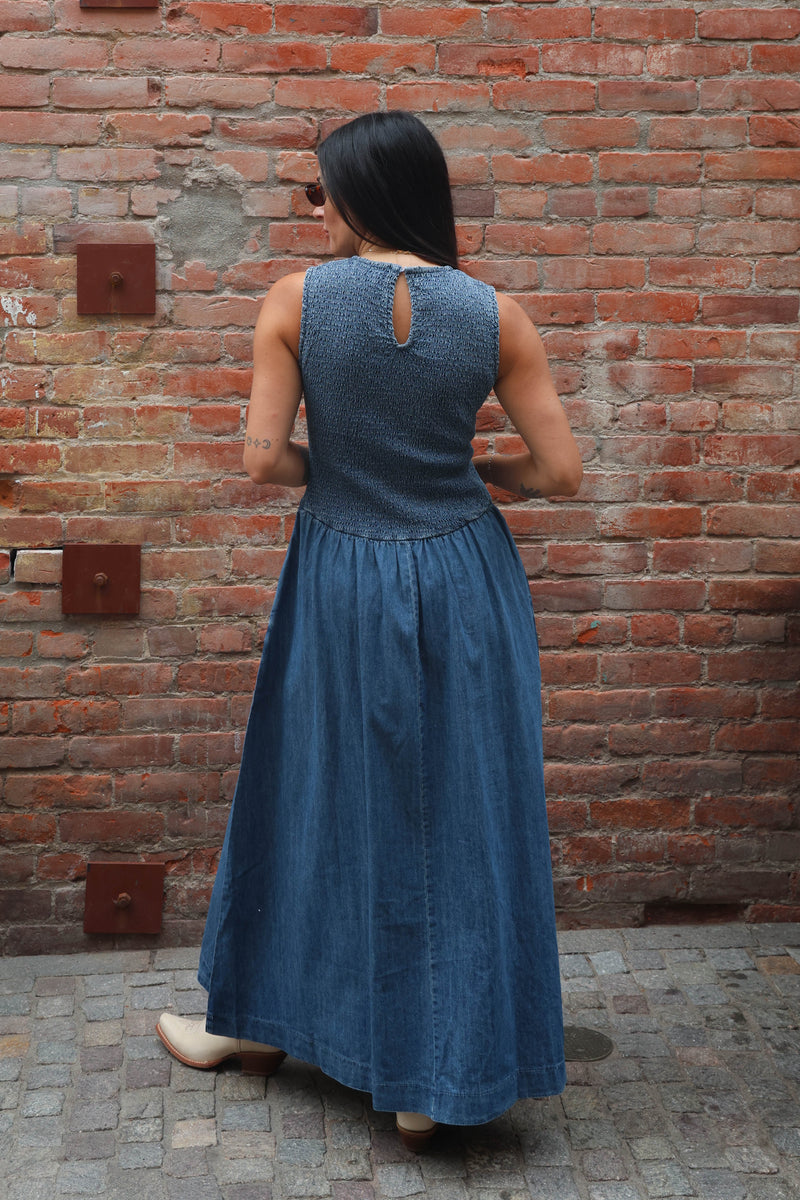 Woman in a blue dress standing against a brick wall.