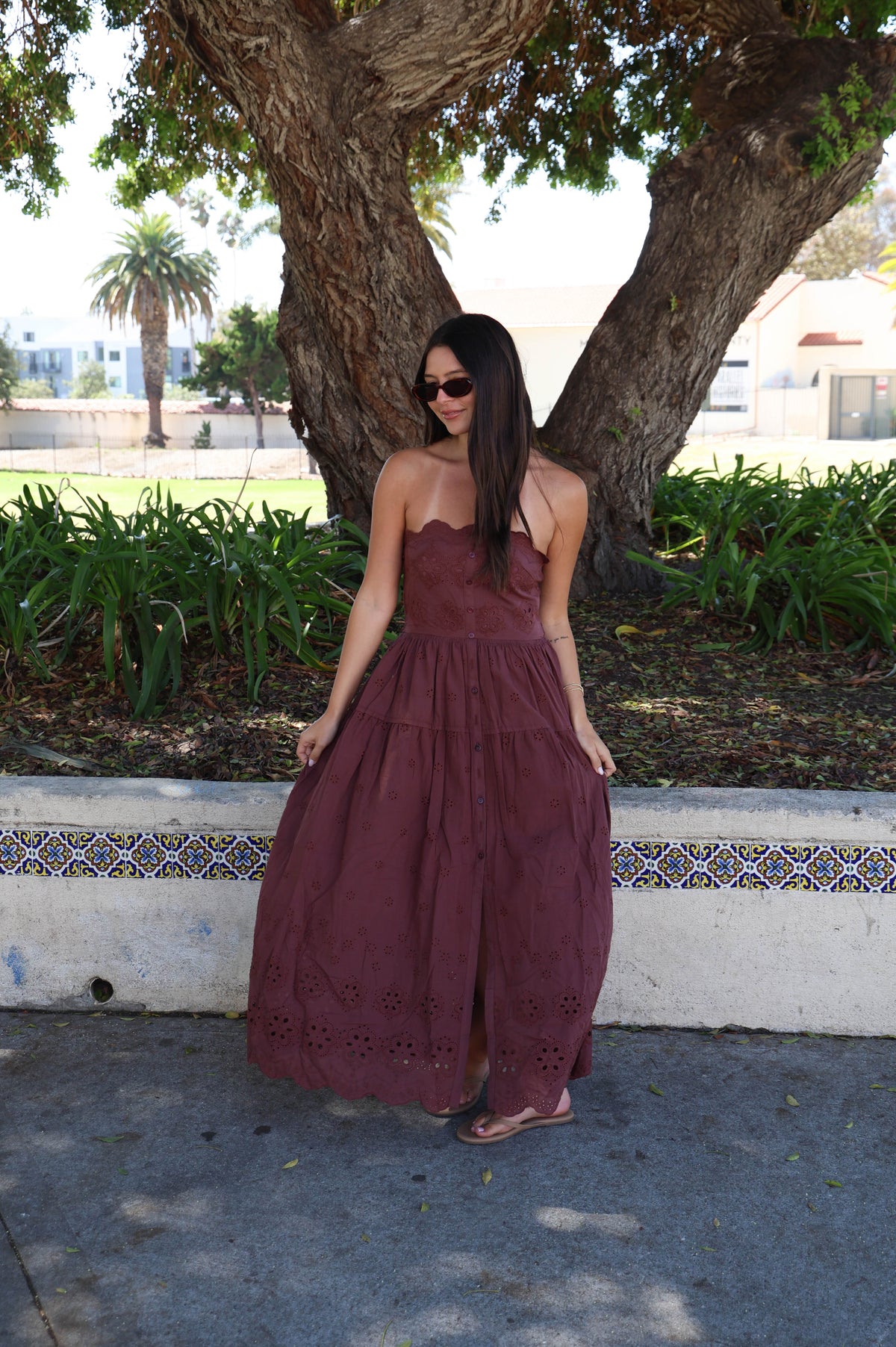 Woman wearing a brown strapless dress in front of a tree.