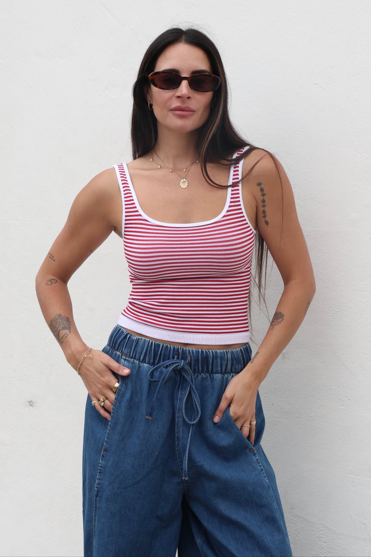 Woman wearing a red and white striped tank top and blue pants against a white background