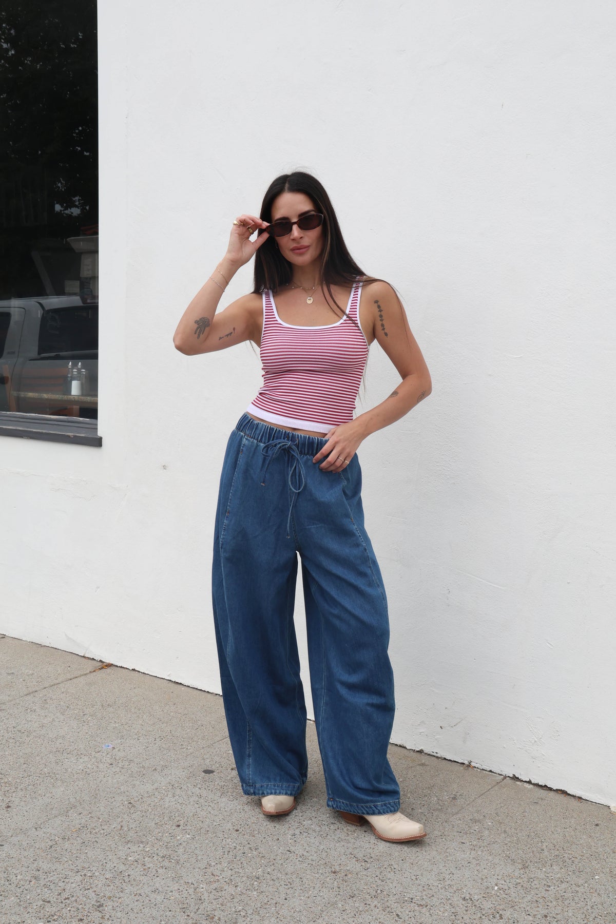 Woman wearing a striped tank top and wide-leg jeans against a white wall.
