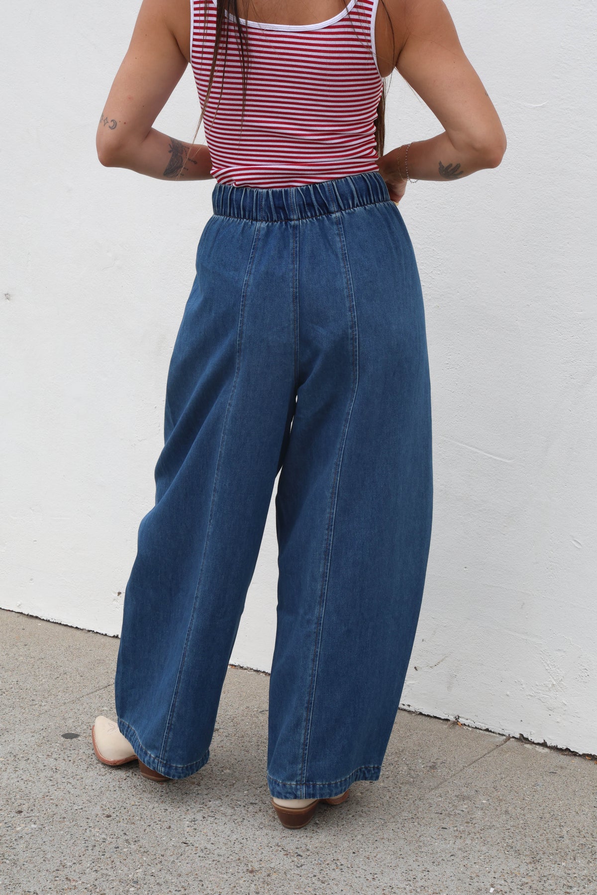 Person wearing a red and white striped tank top and blue wide-leg jeans against a white wall.