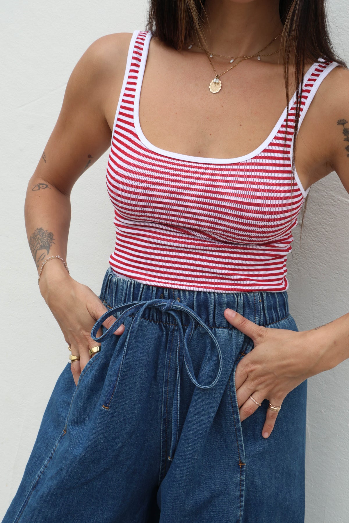 Person wearing a red and white striped tank top and blue jeans against a plain background