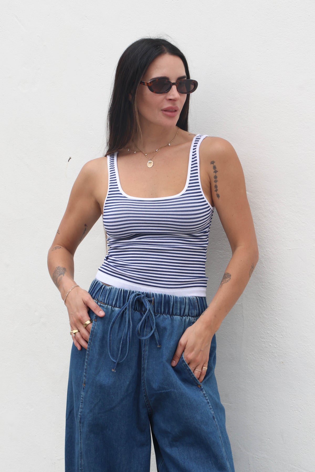 Woman wearing a striped tank top and blue pants against a white wall