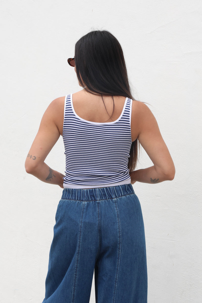 Person wearing a striped tank top and blue jeans against a white background