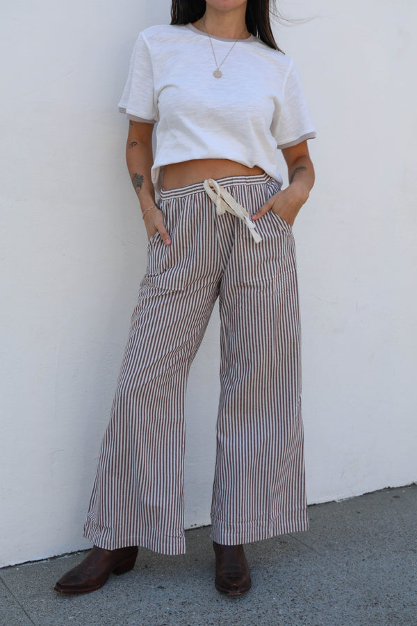 Person wearing a white crop top and striped wide-leg pants against a white wall.