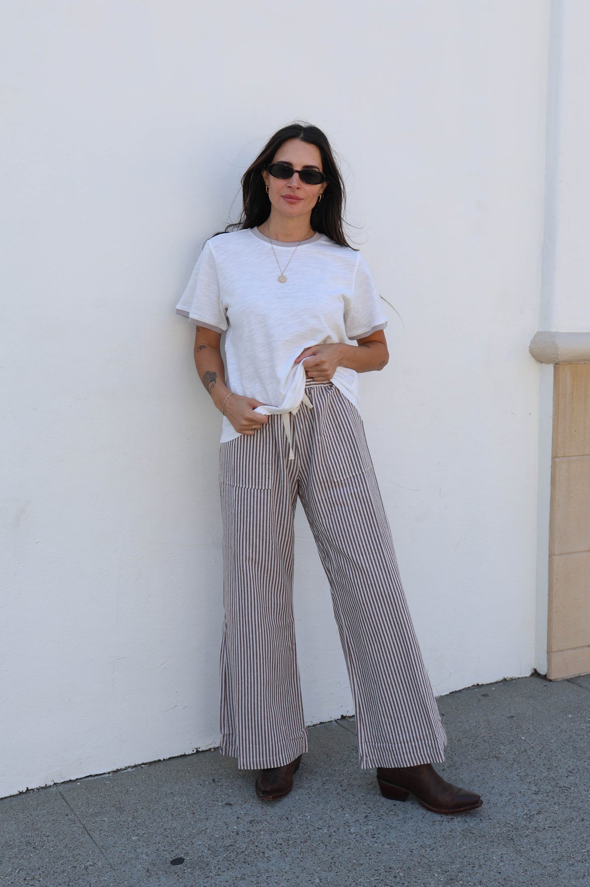 Woman wearing a white t-shirt and striped pants against a white wall.
