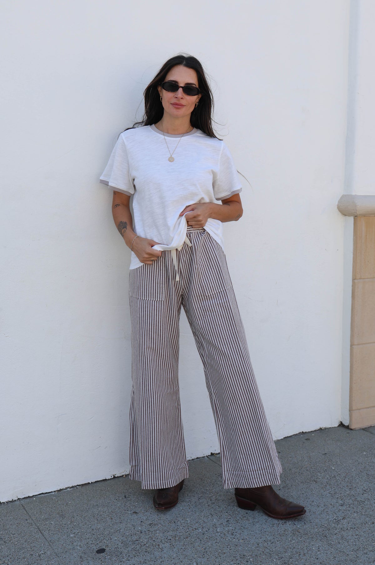 Woman in a white shirt with striped pants against a white wall.