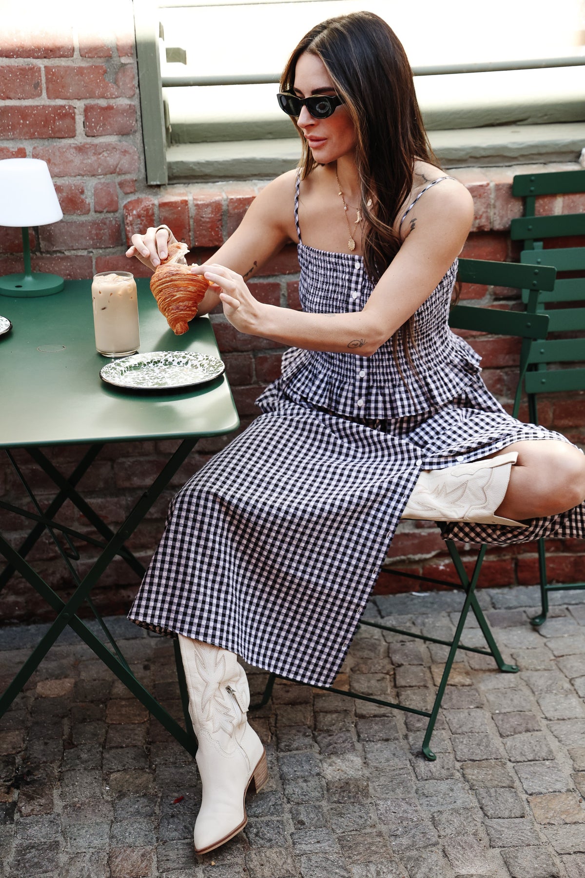 Woman in a checkered dress sitting at an outdoor table, holding a glass of red wine.