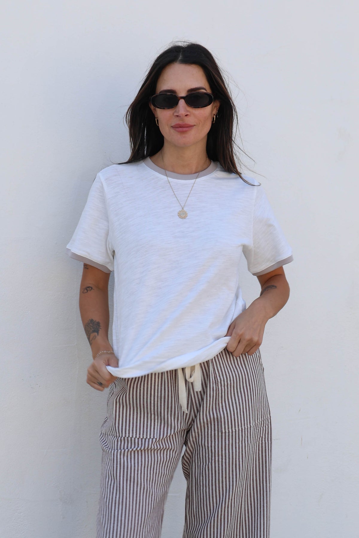 Woman in a white shirt with striped pants against a white wall.
