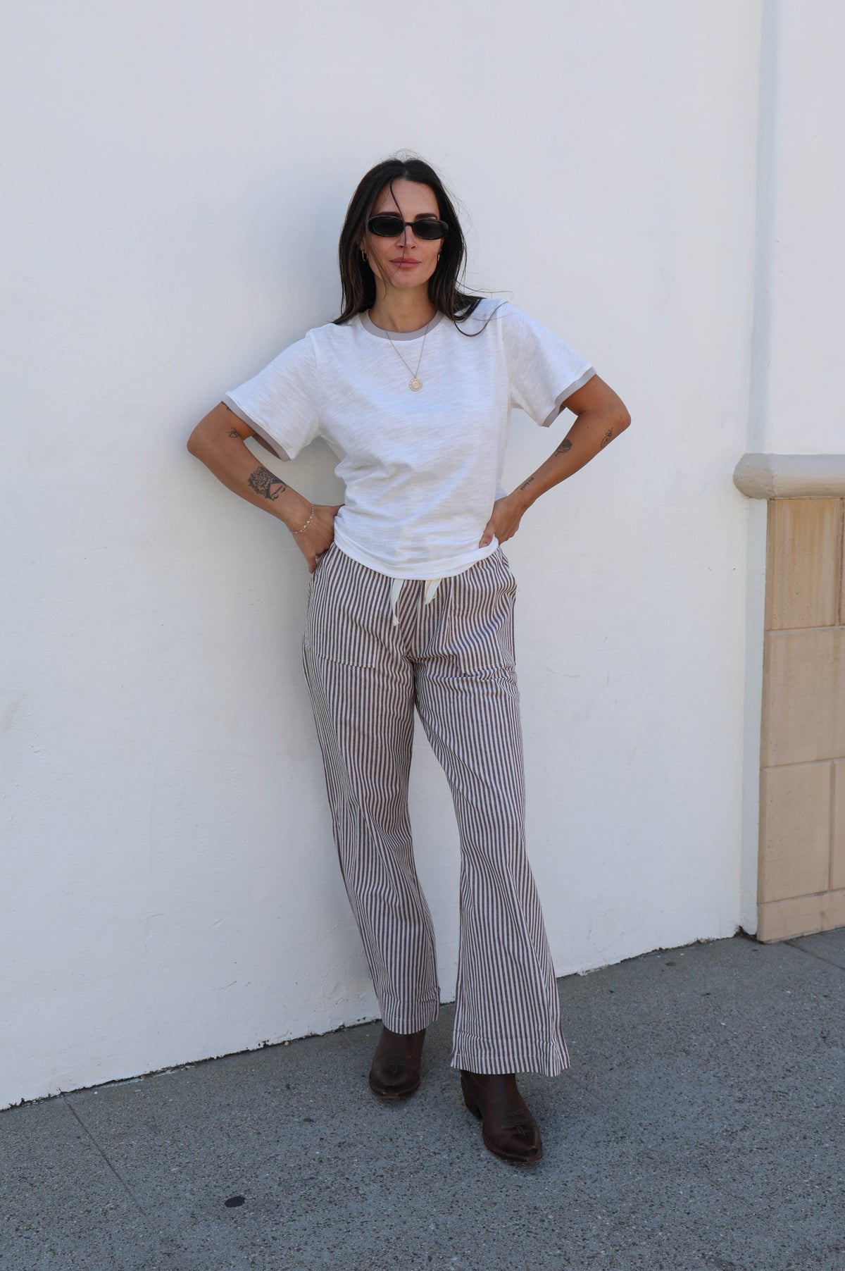 Woman wearing a white t-shirt and striped pants standing against a white wall.