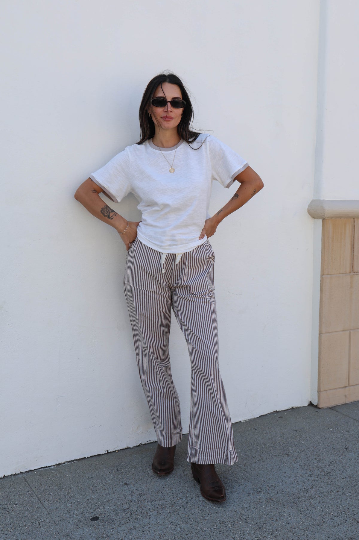 Woman in a white shirt with striped pants against a white wall.