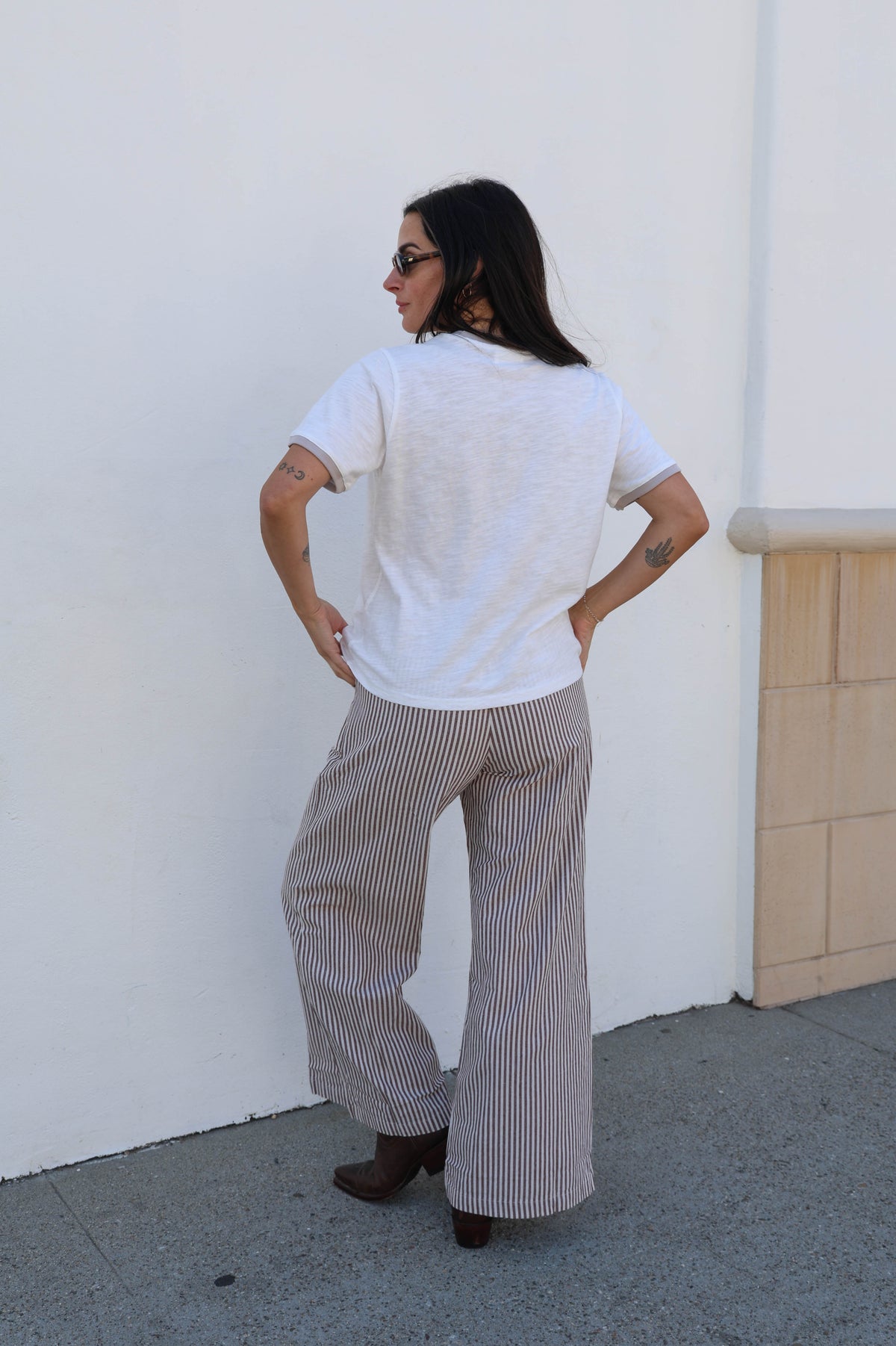 Woman wearing a white t-shirt and striped pants standing against a white wall.