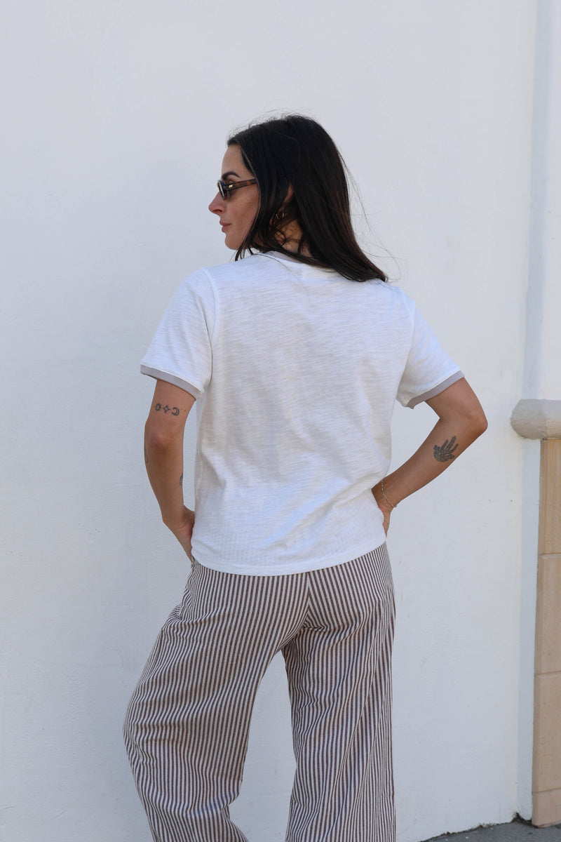 Woman in a white shirt with striped pants against a white wall.