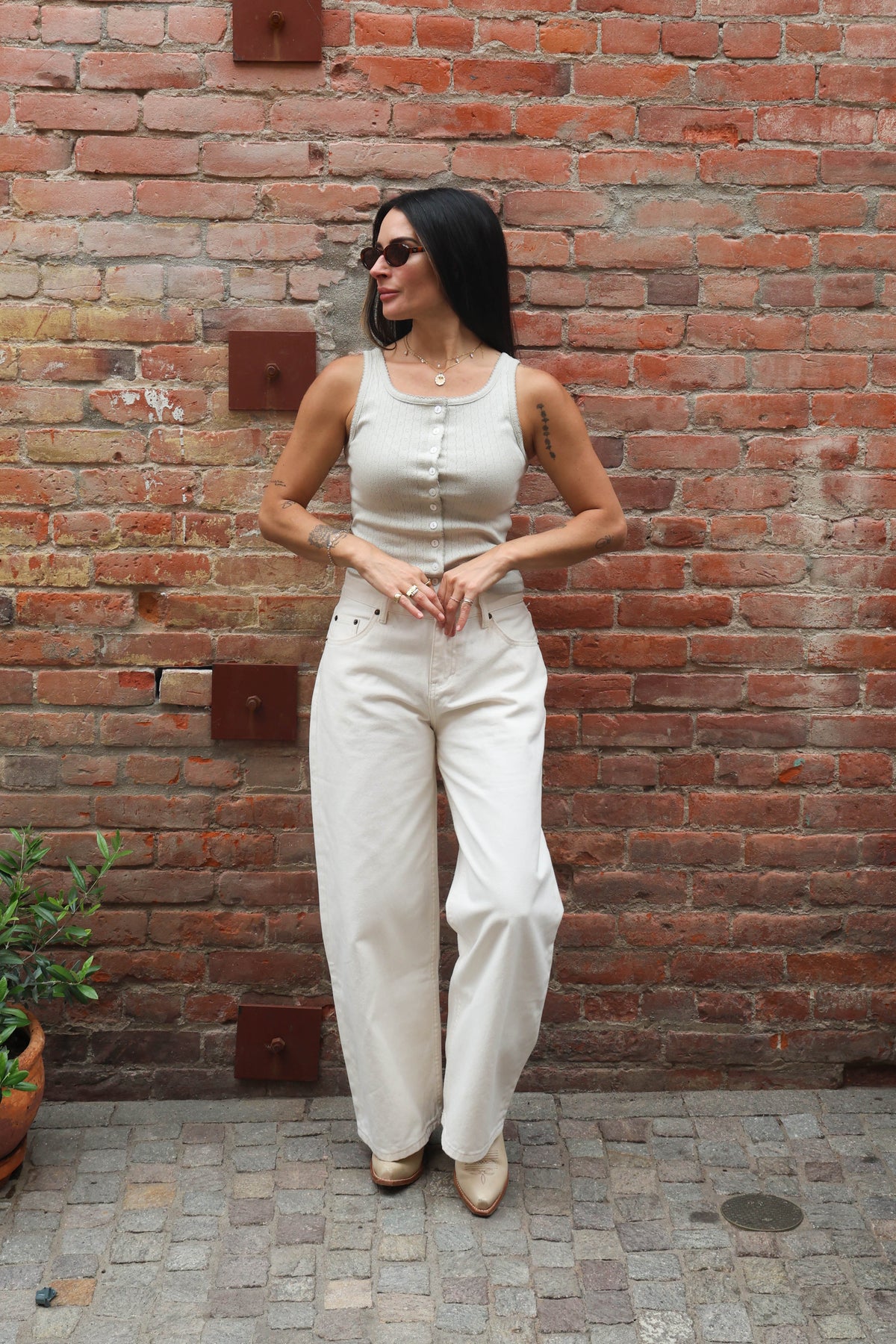 Woman in a white outfit standing against a brick wall