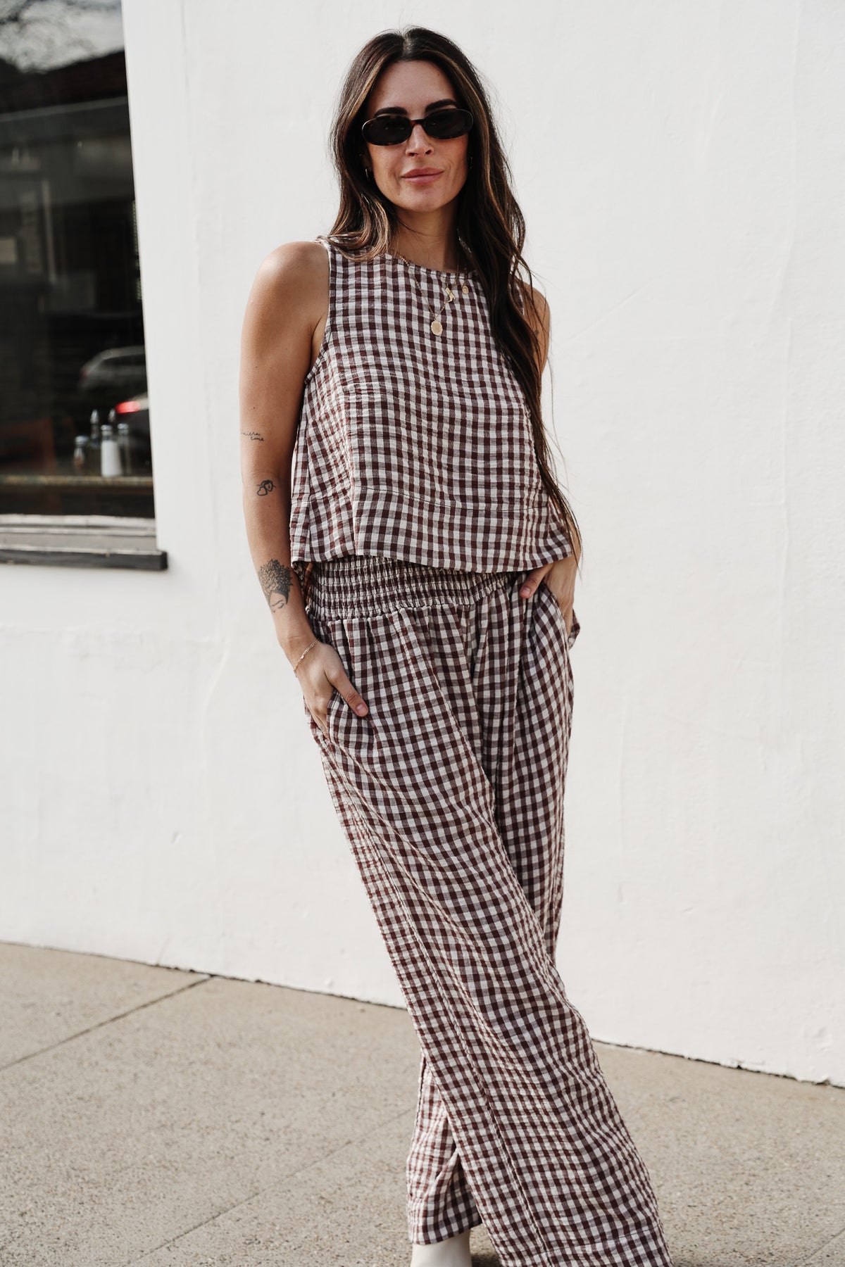 Woman wearing a checkered outfit standing against a white wall.